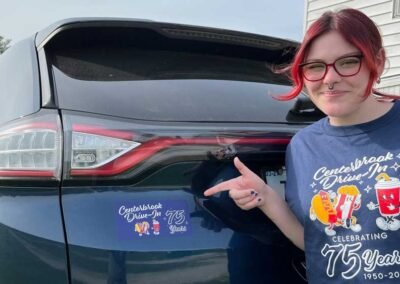 Staff member pointing to 75th Anniversary bumper sticker on a car